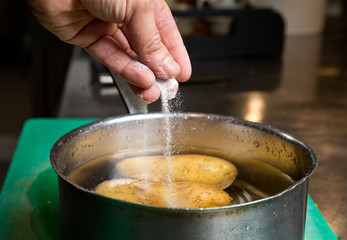 Salt being dropped into a pan of hot water containing potatoes