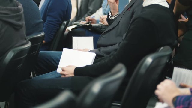 People sitting in business hall at lecture and taking notes - people writing into their notebooks