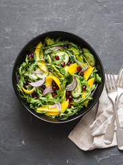 Tropical mango, avocado, cucumber, arugula salad. Delicious healthy vegetarian food. On a dark background, top view