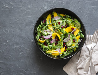 Tropical mango, avocado, cucumber, arugula salad. Delicious healthy vegetarian food. On a dark background, top view