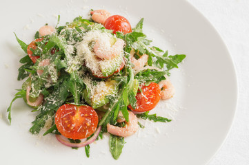 green salad with cherry tomatoes, prawns, avocado, and red onion sprinkled with grated cheese