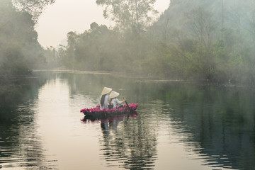 River scene with smoke, a boat carrying girls wearing traditional dress Ao Dai, conical hat, and flower.