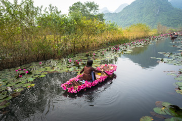 Vietnam landscape with woman rowing boat loaded with flowers on Yen stream, Ninh Binh, Vietnam