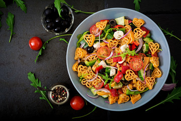 Pasta in the shape heart salad with tomatoes, cucumbers, olives, mozzarella and red onion Greek style. Flat lay. Top view