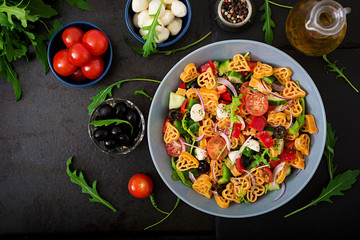 Pasta in the shape heart salad with tomatoes, cucumbers, olives, mozzarella and red onion Greek style. Flat lay. Top view