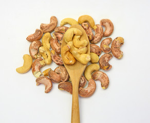 Cashew nuts in a wooden spoon against pile of cashew nut on white background