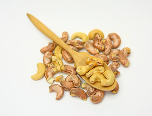 Cashew nuts in a wooden spoon against pile of cashew nut on white background
