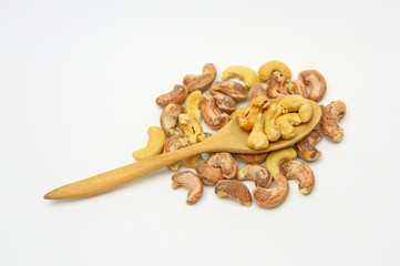 Cashew nuts in a wooden spoon against pile of cashew nut on white background