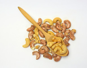 Cashew nuts in a wooden spoon against pile of cashew nut on white background