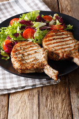 Grilled pork chop with fresh vegetable salad close-up on table. Vertical