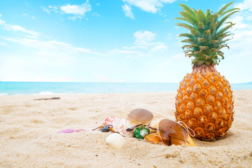 Fototapeta na wymiar Ripe pineapples and sunglasses, seashell on the sandy tropical beach with clear blue sky. Leisure in summer and Summer vacation concept. vintage color tone.