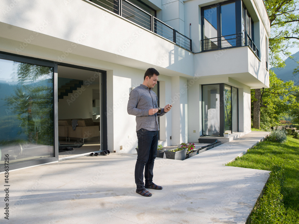 Wall mural man using mobile phone in front of his luxury home villa