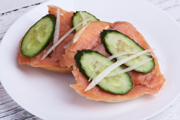 Bagel with salmon, cucumber, onion on white plate. Front view.