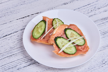 Bagel with salmon, cucumber, onion on white plate. Front view.