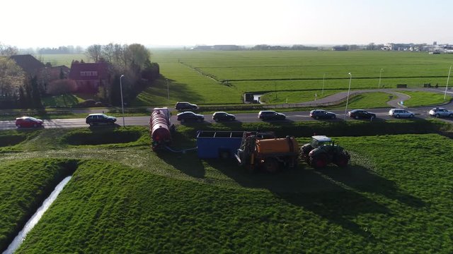 Aerial flight bird view near large truck and farmer in tractor showing the truck distributing feces manure to tractor for fertilizing grassland in background showing heavy traffic and roundabout 4k