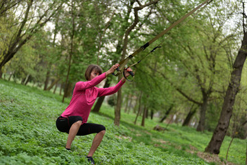 Obraz na płótnie Canvas Beautiful young woman doing TRX exercise with suspension trainer sling in the outdoors