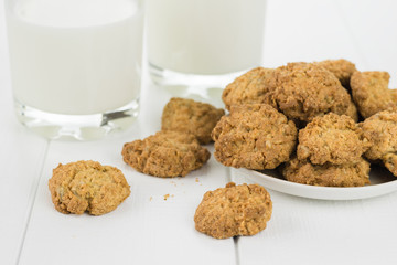 A bowl with homemade cookies and two glasses of milk on a wooden table.