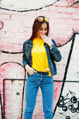 Beautiful teenage girl wear yellow t-shirt and jeans near graffiti wall.