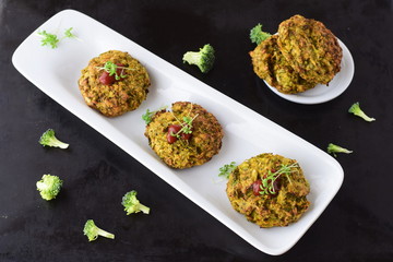 Broccoli balls deep fried on a white plate with tomato sauce with fresh broccoli on a black abstract background. Healthy eating concept. Dieting