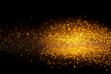 Fototapeta premium Sprinkle gold glitter dust on a black background with copy space.