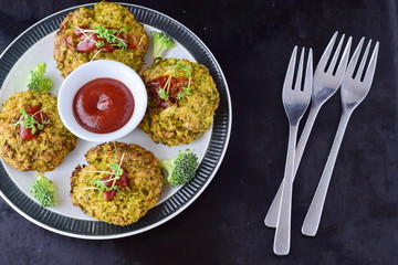 Broccoli balls deep fried on a white plate with tomato sauce with fresh broccoli on a black abstract background. Healthy eating concept. Dieting