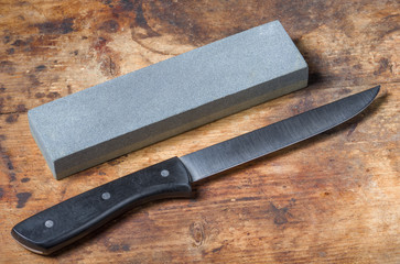 Knife and whetstone on the old wooden cutting board