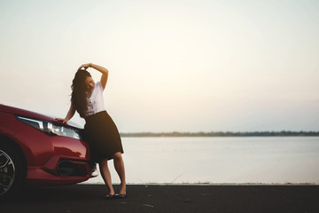 young woman happy standing in front of the red car with sunset on the park