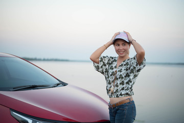 young woman standing in front of the red car with sunset on the park