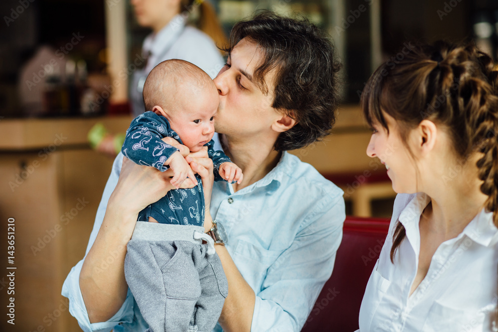 Wall mural lovely family with newborn baby in cafe. happy father kissing the little son. fatherhood and family 