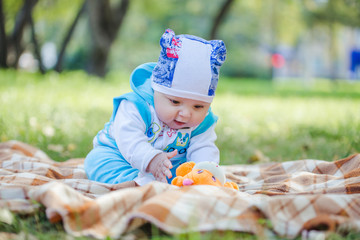 Малыш сидит на пледе в парке и играет с игрушкой. © 89502687345