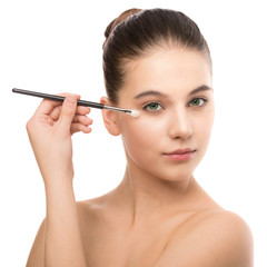 Fototapeta premium Portrait of beautiful young brunette woman with clean face. Beauty spa model girl with perfect fresh clean skin applying cosmetic brush. Youth and skin care concept. Isolated on a white background.