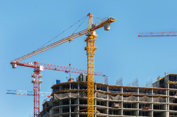 Construction site. Construction cranes and high-rise building under construction against blue sky.