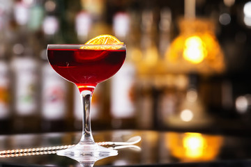 Glass of cherry color alcohol cocktail decorated with orange slice at bar counter backgound.