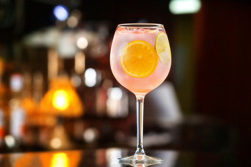 Glass of pink alcohol cocktail decorated with lemon slices at bar counter background.