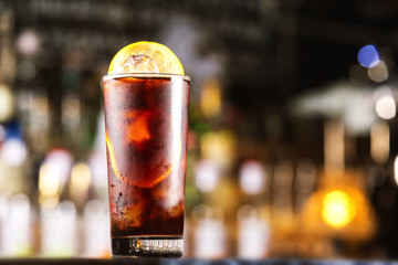 Rum cola cocktail with ice cubes and lemon at festive bar stand background.