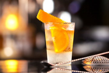 Closeup glass of old fashioned cocktail decorated with orange at bar counter background.