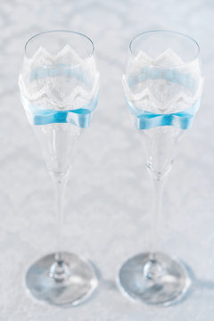 Glasses of wine glasses. The transparent glasses are decorated with white lace and blue ribbon. Vertical frame, selective focus.