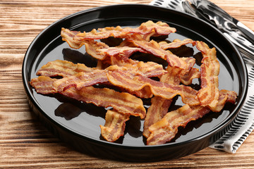 Plate with tasty bacon slices on wooden background
