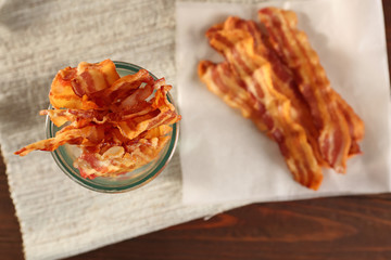 Tasty bacon slices in glass cup on table