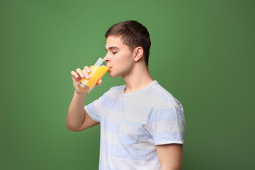 Young man drinking juice on color background