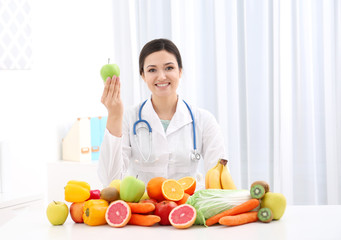 Female nutritionist with different fruits and vegetables at desk
