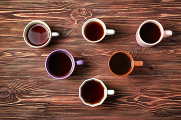Delicious tea in cups forming triangle on wooden background