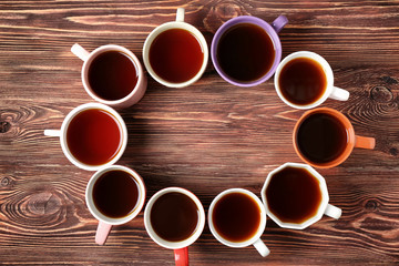 Delicious tea in cups forming circle on wooden background