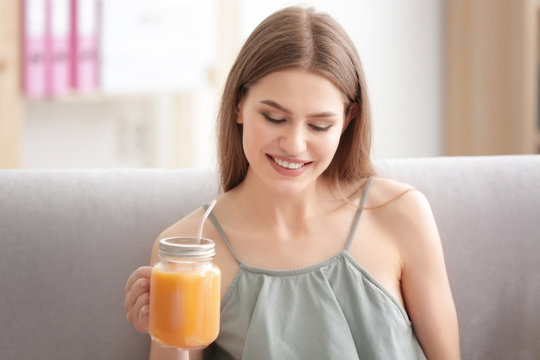 Young woman tasting fresh juice sitting on couch at living room