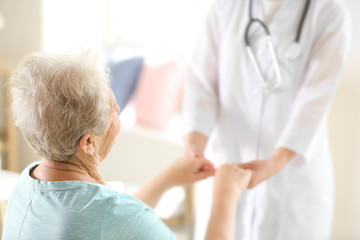 Obraz premium Young doctor holding hands of elderly woman on light background