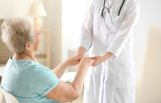 Young doctor holding hands of elderly woman on light background