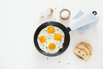 Fried scrambled eggs in a frying pan, bread and salt on a white background.