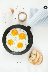 Fried scrambled eggs in a frying pan, bread and salt on a white background.