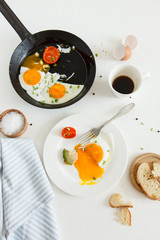 Eating in the process, fried eggs in a frying pan and on a plate, toast with avocado and a cup of coffee for breakfast.