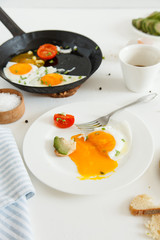 Eating in the process, fried eggs in a frying pan and on a plate, toast with avocado and a cup of coffee for breakfast.